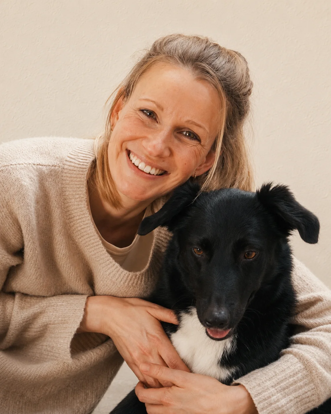 Sylvia Schreiber, Tierphysiotherapeutin und Tierosteopathin aus Neuss, lächelt mit dem Arm um einen schwarzen Hund mit weißer Brust