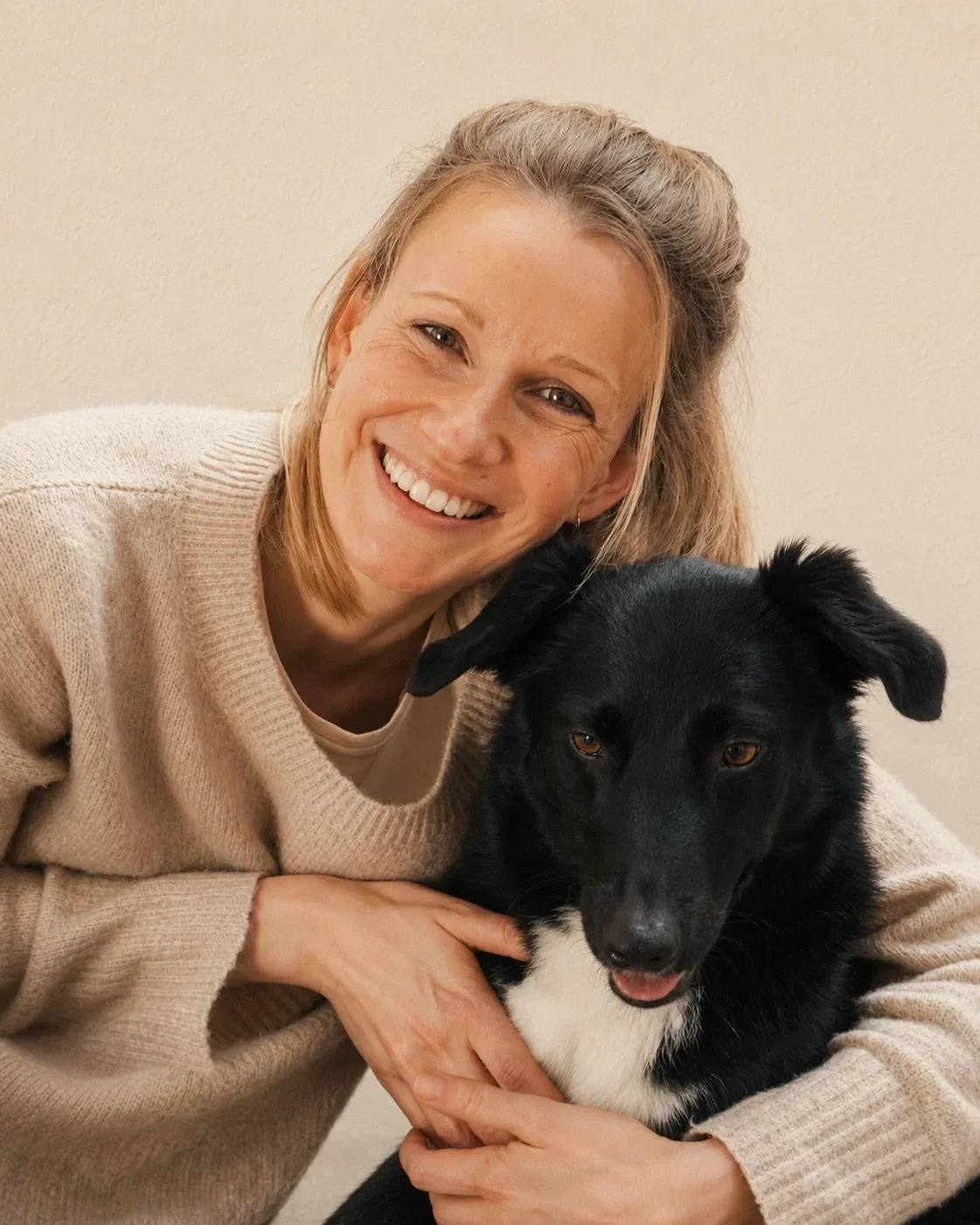 Sylvia Schreiber, Tierphysiotherapeutin für Hunde und Kleintiere und Hundeosteopathin aus Neuss, lächelt mit dem Arm um ihre Hündin Muri, schwarz mit weißer Brust